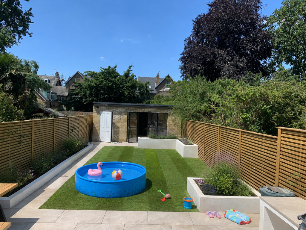 Freshly turfed London garden with paddling pool, children’s toys, wooden fencing and raised flower beds